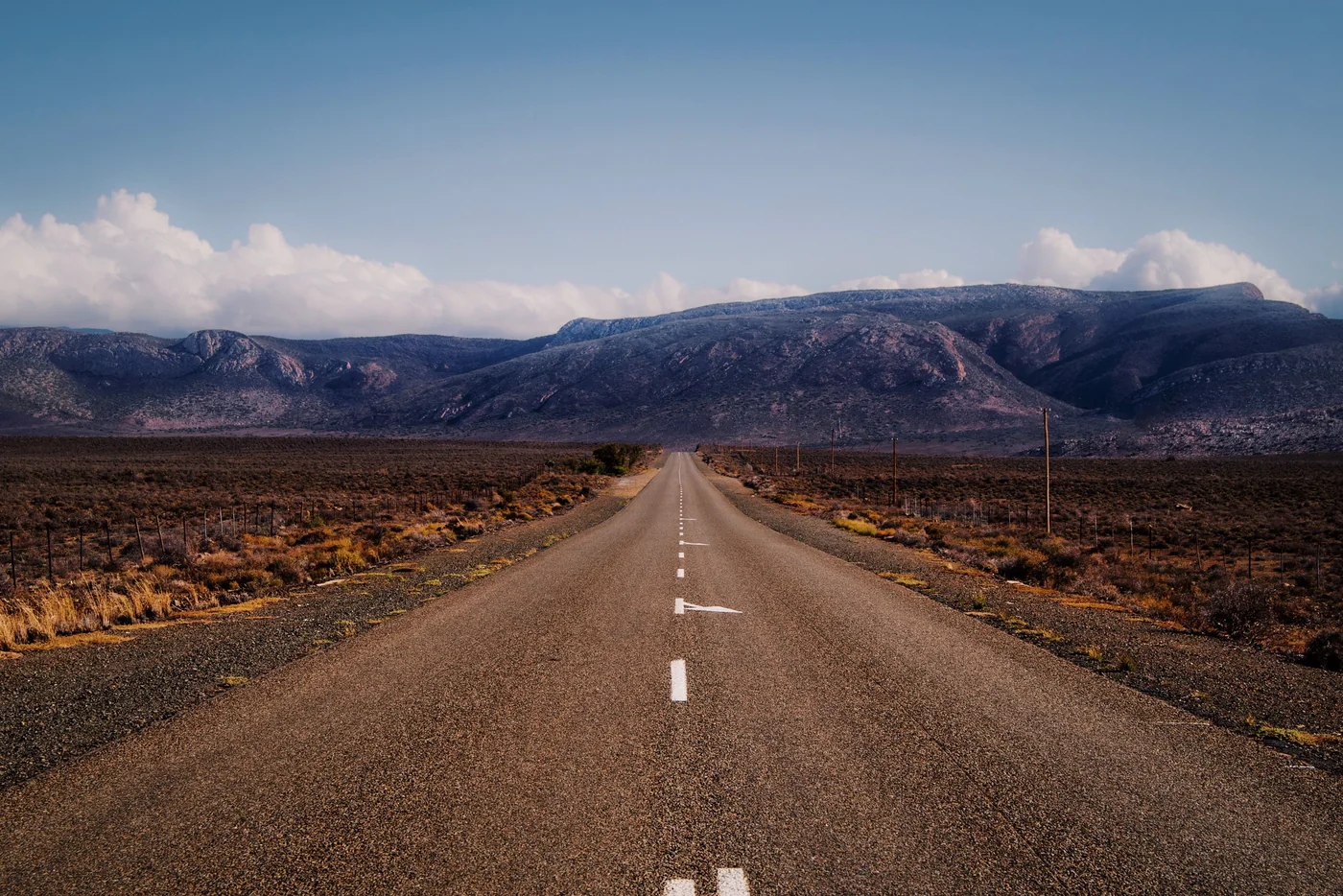 An empty two-lane road running straight toward mountains through Karoo scrubland, Western Cape